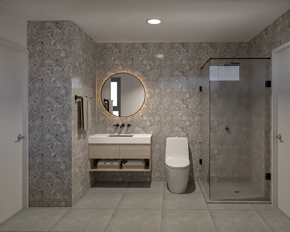 Baño moderno con paredes de terrazo, espejo redondo retroiluminado y ducha con mampara.